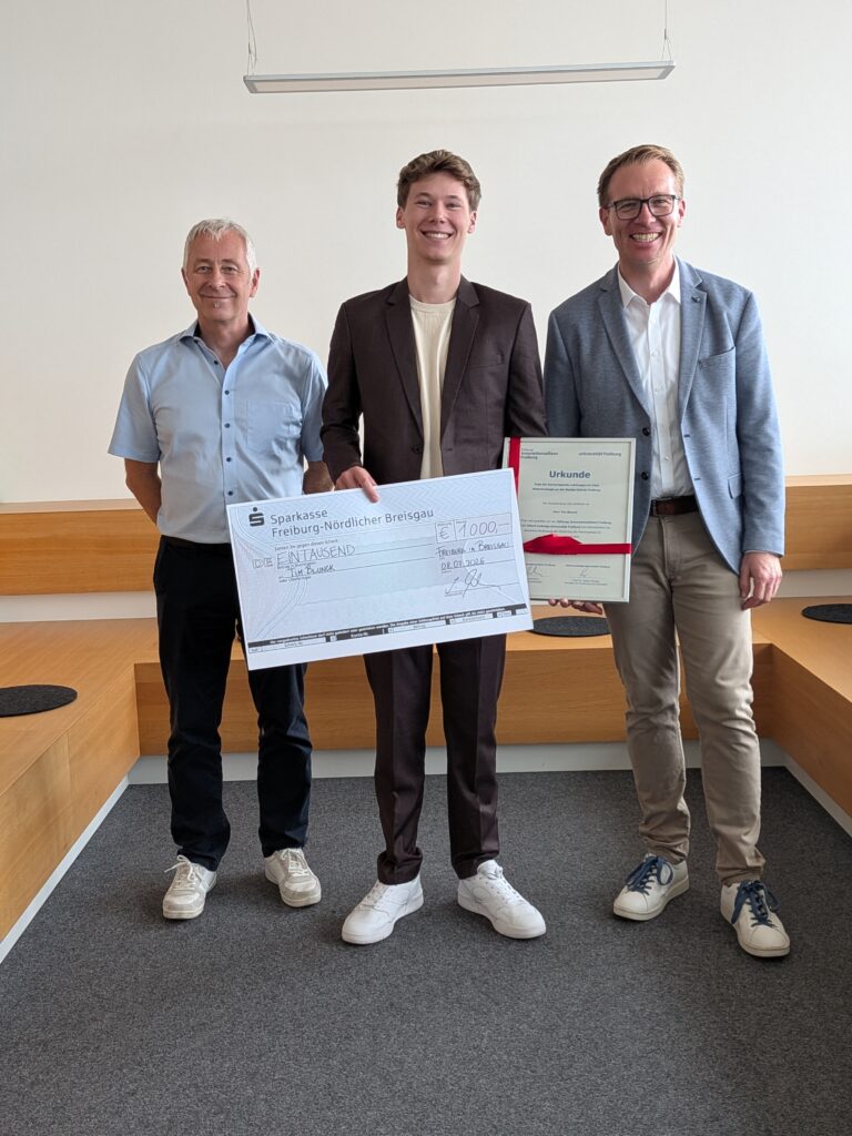 Three men stand indoors, posing with a large check and a framed certificate after a donation award event.