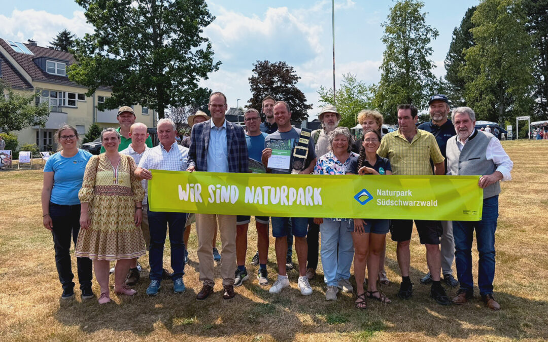 Group of people standing outdoors holding a bright yellow banner that reads 'WIR SIND NATURPARK' with 'Naturpark Südschwarzwald' logo on the right.