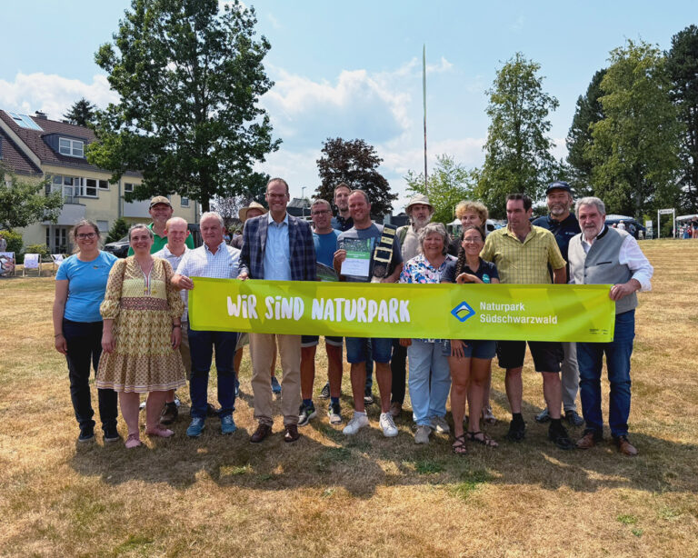 Group of people standing outdoors holding a bright yellow banner that reads 'WIR SIND NATURPARK' with 'Naturpark Südschwarzwald' logo on the right.