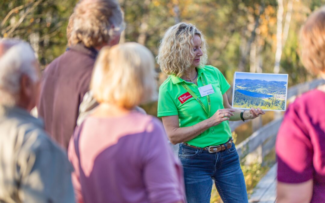 Woman in a bright green shirt presents a landscape photo to a small group outdoors.