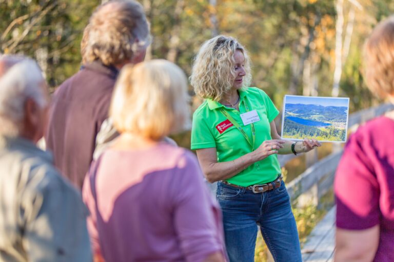 Woman in a bright green shirt presents a landscape photo to a small group outdoors.