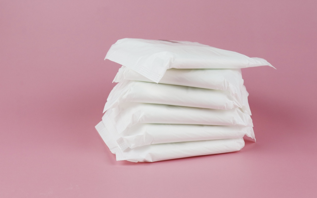 Stack of white sanitary pads arranged in a tall pile on a pink backdrop
