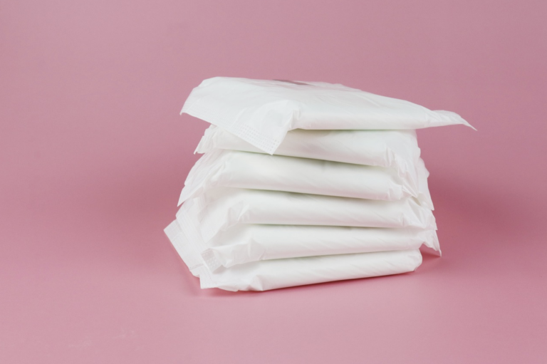 Stack of white sanitary pads arranged in a tall pile on a pink backdrop