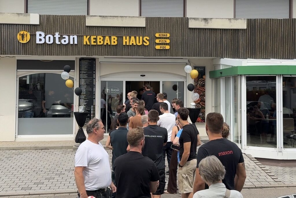 Line of people waiting to enter Botan Kebab Haus restaurant with balloons outside the storefront.
