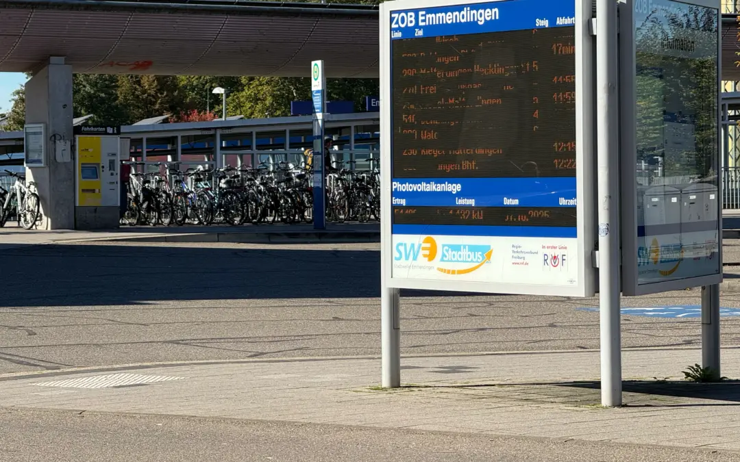 Bus stop with a large electronic timetable display and blue ZOB Emmendingen sign; bicycle racks visible nearby under a shelter.