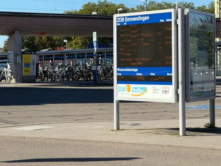 Bus stop with a large electronic timetable display and blue ZOB Emmendingen sign; bicycle racks visible nearby under a shelter.
