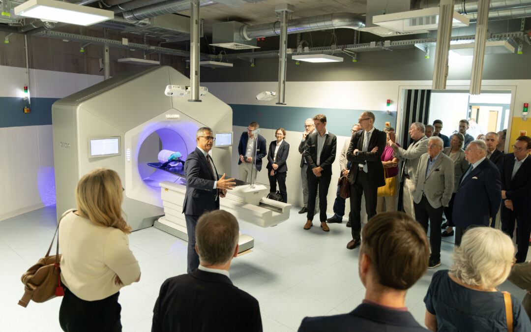 Professionals in business attire observe a large medical imaging machine in a clinical lab during a demonstration tour.