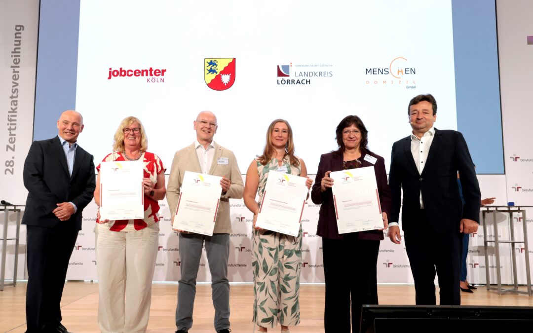 Six adults on a stage holding certificates at a formal awards ceremony, smiling for the photo.
