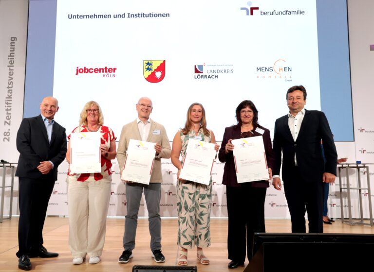 Six adults on a stage holding certificates at a formal awards ceremony, smiling for the photo.
