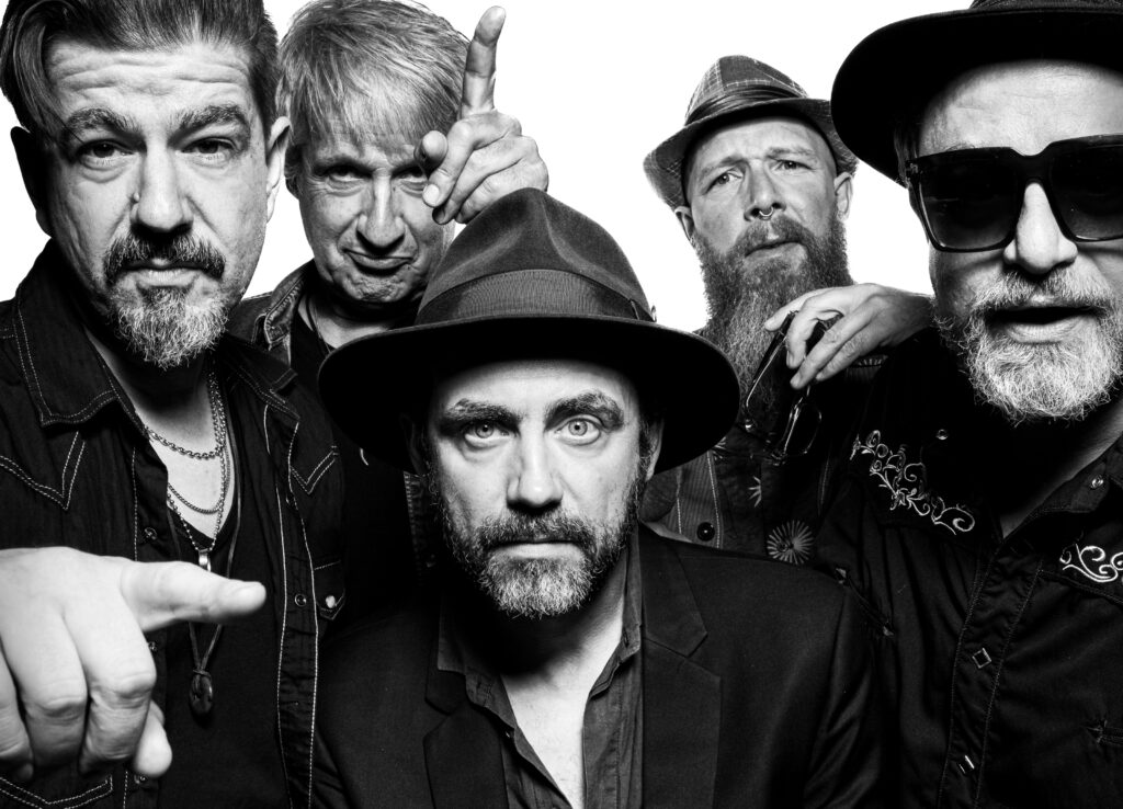 Close-up group shot of five men in a rock band posing for a black-and-white photo, one pointing toward the camera.