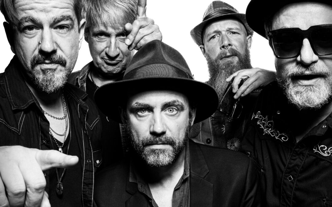 Close-up group shot of five men in a rock band posing for a black-and-white photo, one pointing toward the camera.