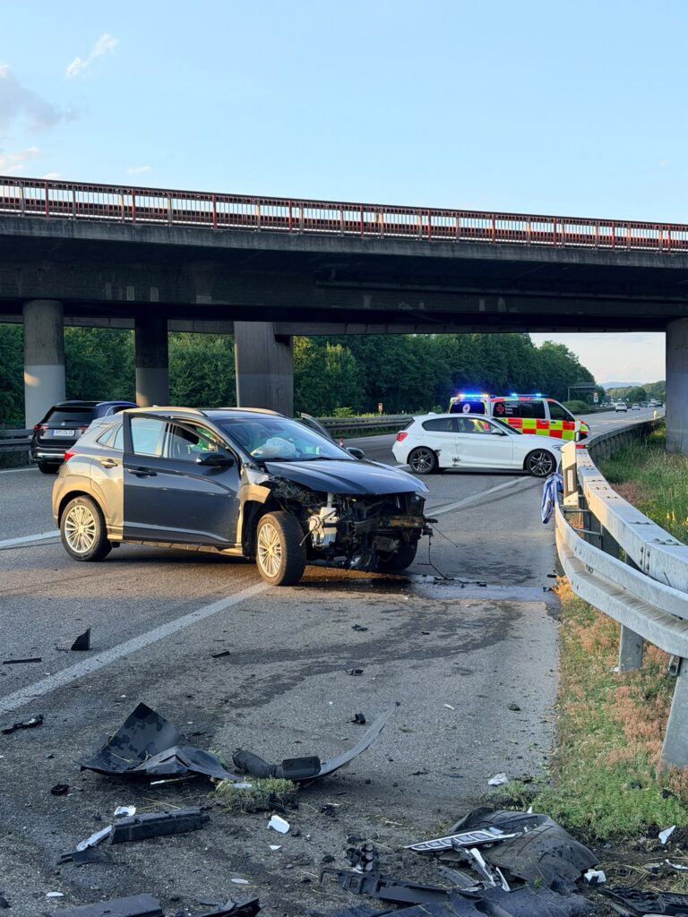 Cars involved in a multi-vehicle crash on a highway under an overpass, with debris scattered on the road and emergency vehicles in the distance