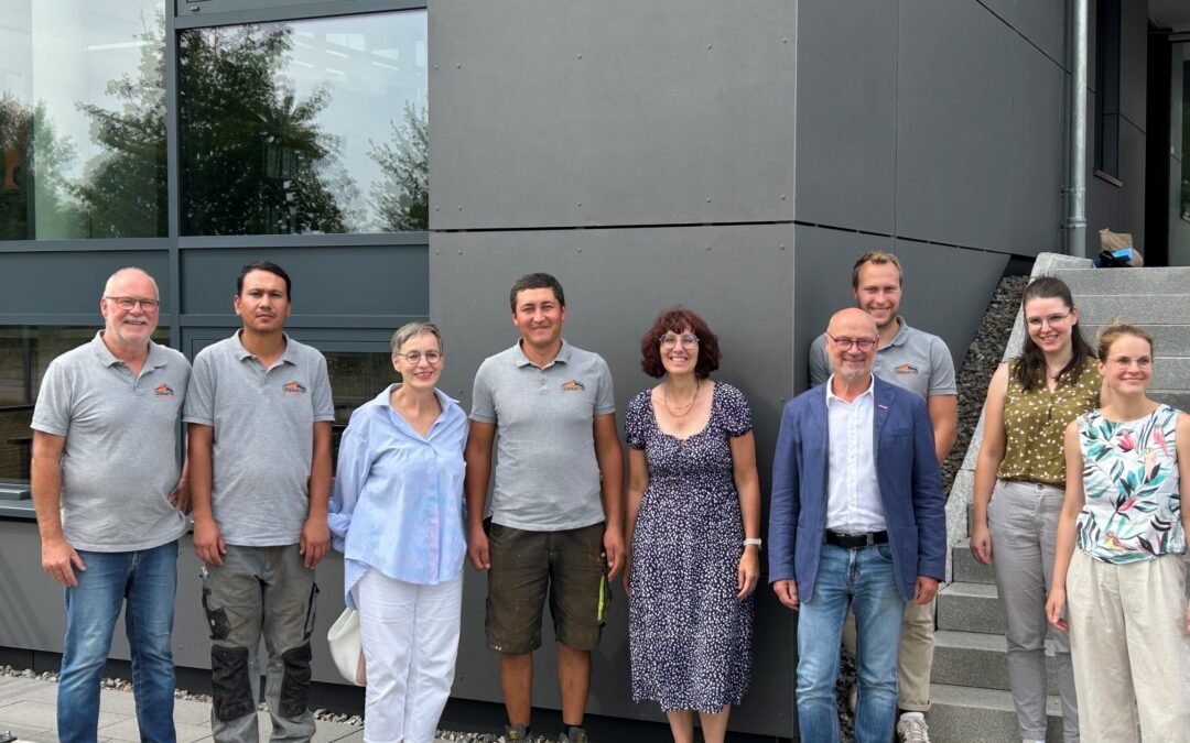 Group of people posing for a photo outside a modern gray building, smiling at the camera.