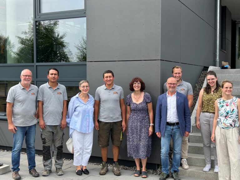 Group of people posing for a photo outside a modern gray building, smiling at the camera.