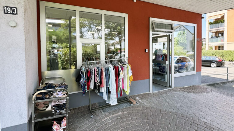 Outdoor storefront with clothing racks and shoe displays outside a red building on a cobblestone sidewalk.