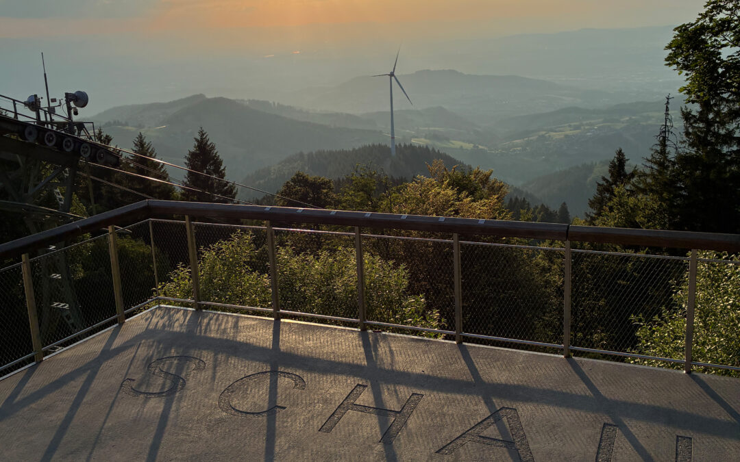 Observation deck overlooking a hazy valley with a distant wind turbine and sun rays in a golden sky.
