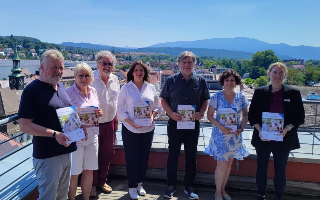 Group of adults standing on a rooftop terrace holding brochures, with a town and distant hills in the background on a sunny day.