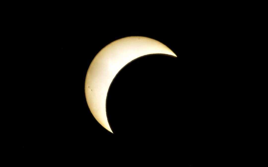 Pale crescent sun glowing against a black night sky during a partial solar eclipse in silhouette.
