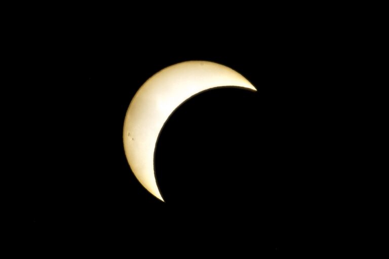 Pale crescent sun glowing against a black night sky during a partial solar eclipse in silhouette.