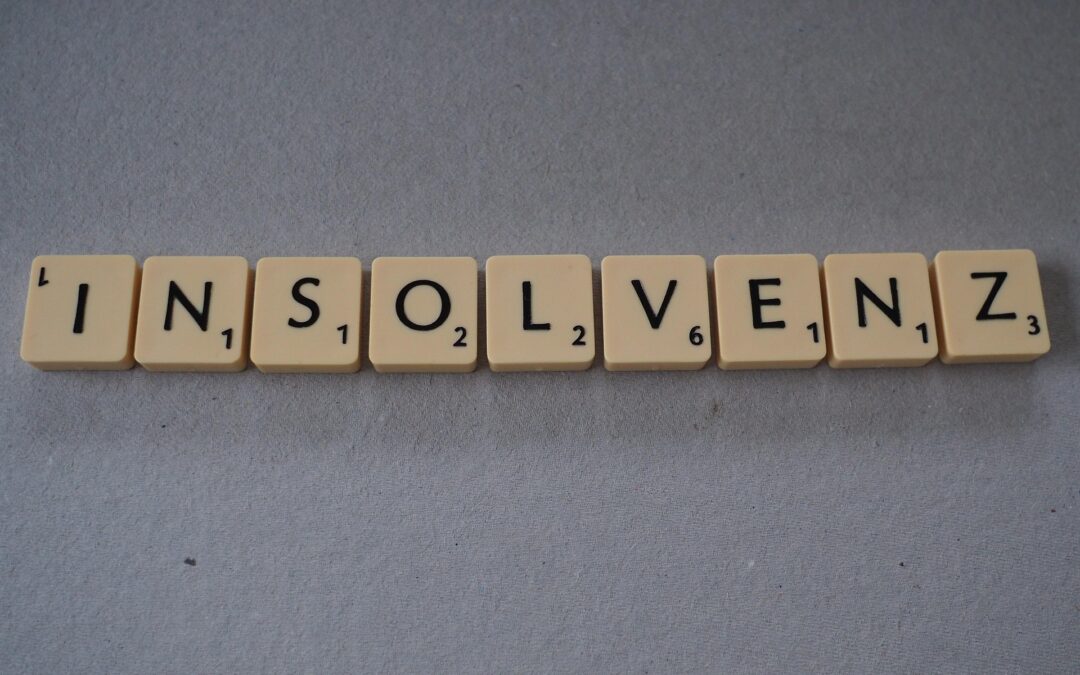 Row of Scrabble tiles spelling 'INSOLVENZ' on a gray surface.