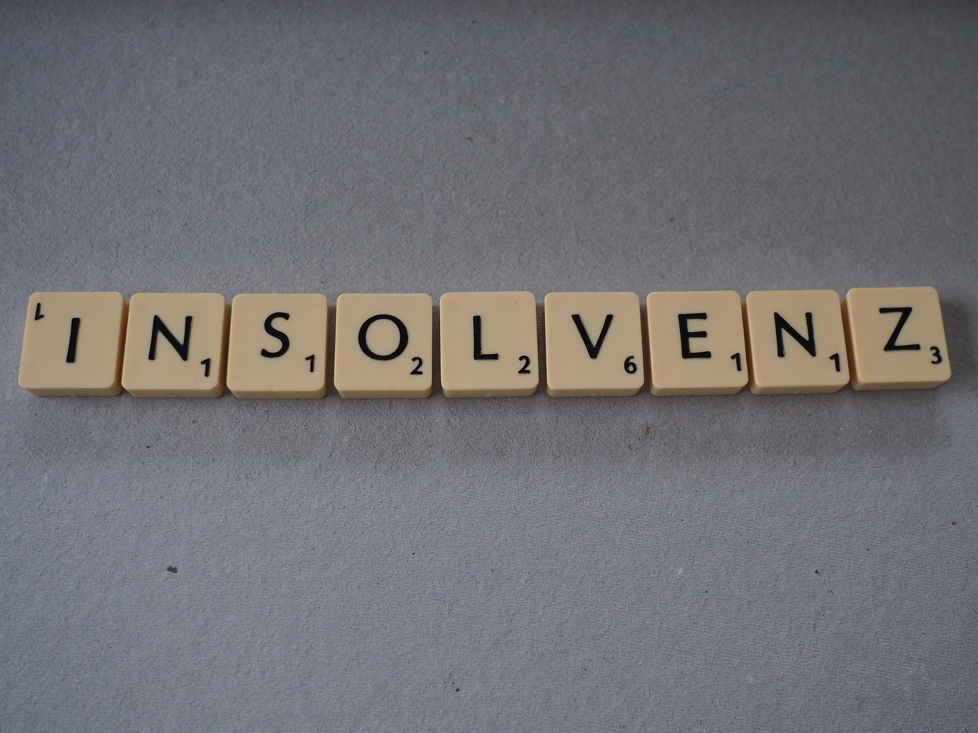Row of Scrabble tiles spelling 'INSOLVENZ' on a gray surface.