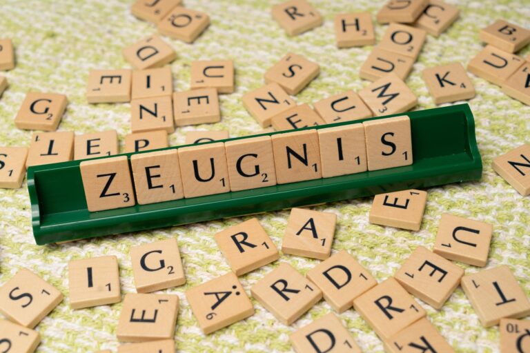 Scrabble tiles on a green rack spell 'ZEUGNIS' on a patterned surface.