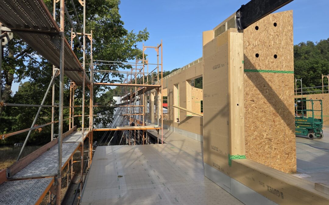 Construction site with metal scaffolding along a wooden formwork wall under clear blue skies.