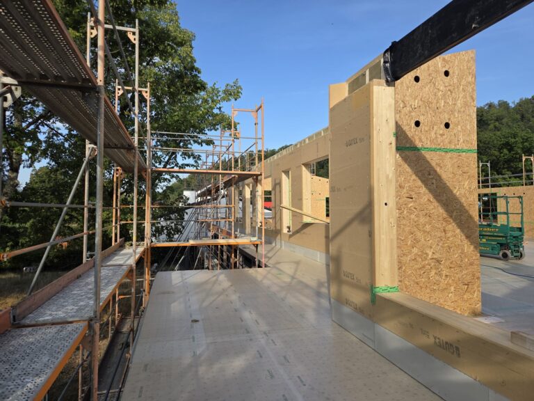 Construction site with metal scaffolding along a wooden formwork wall under clear blue skies.