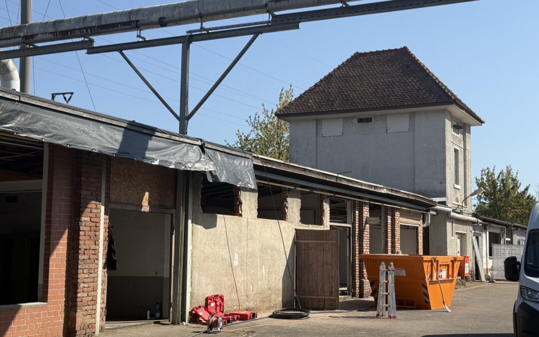 Industrial building with overhead metal pipes and scaffolding, construction barriers, and hoses on a sunny day