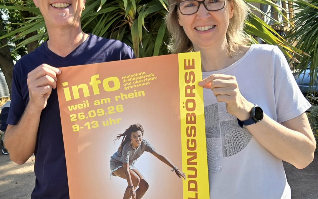 Two smiling adults wearing glasses hold an orange poster outdoors, with a large yellow stripe and palm plants in the background.