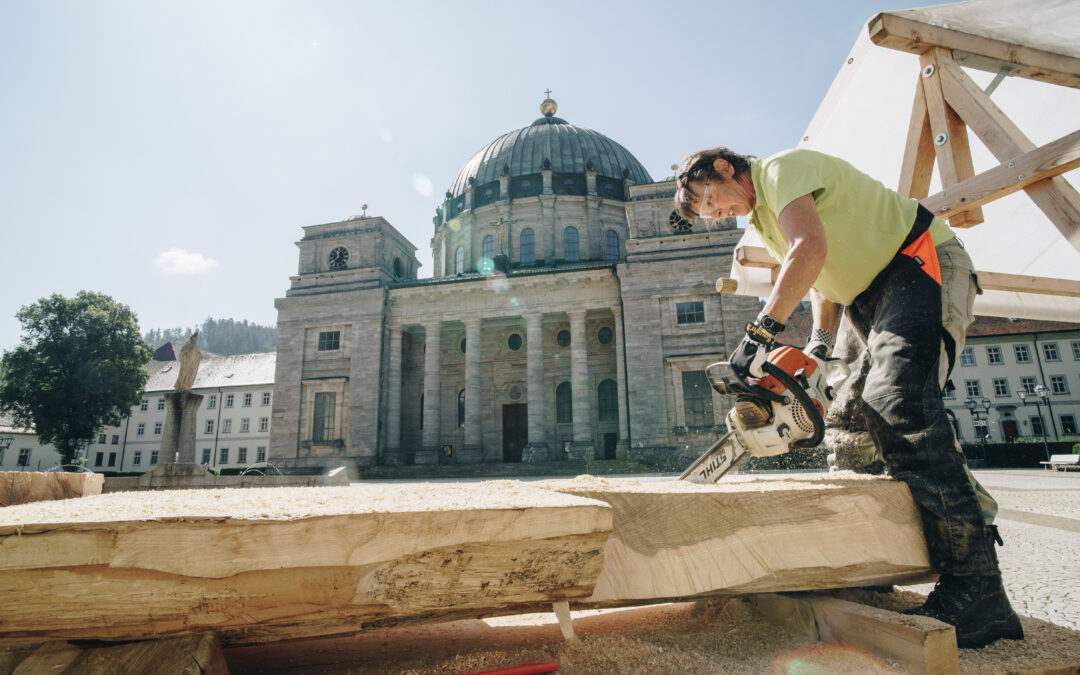 Construction worker cutting a wooden beam with a power saw in front of a historic cathedral.