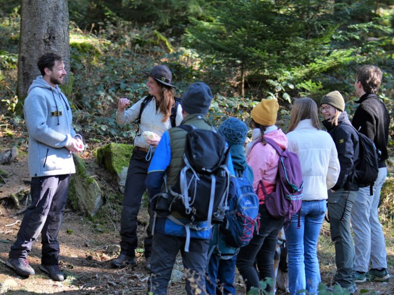 Group of hikers with backpacks listening to a guide in a forest setting.