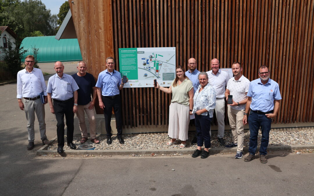 Group of eleven adults posing outdoors beside a large map display mounted on a wooden slat wall.