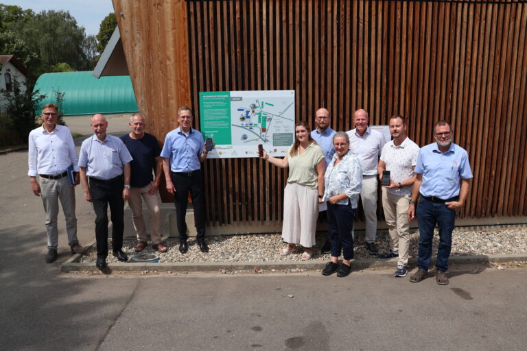 Group of eleven adults posing outdoors beside a large map display mounted on a wooden slat wall.