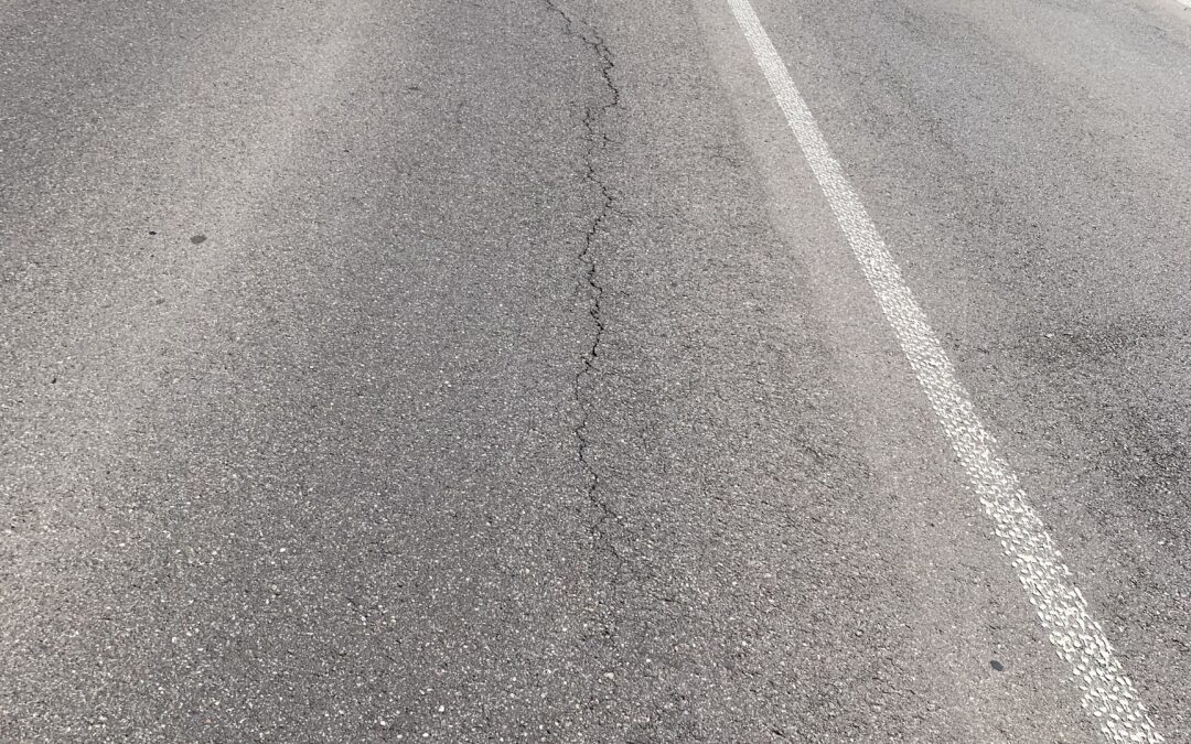 Rural two-lane road curves to the left with a white center line and grassy shoulders on both sides.