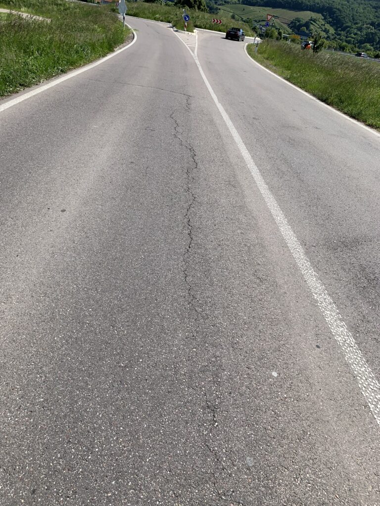 Rural two-lane road curves to the left with a white center line and grassy shoulders on both sides.
