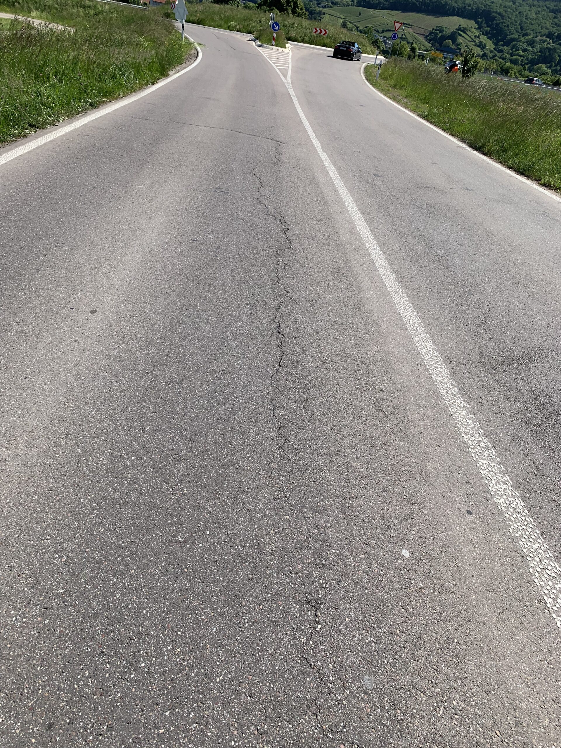 Rural two-lane road curves to the left with a white center line and grassy shoulders on both sides.