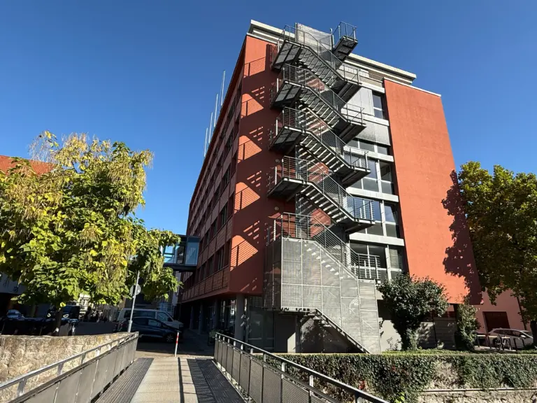 Red brick apartment building with a metal exterior fire escape zigzagging down the façade against a clear blue sky.