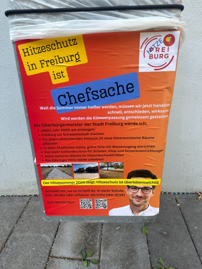 Orange poster on a trash can promoting heat protection in Freiburg; features a blue 'Chefsache' label and a portrait photo at the bottom.