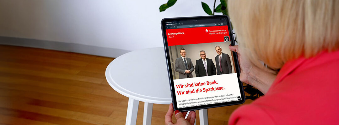 Person in a red jacket holds a tablet showing a Sparkasse advertisement with three men in suits on a red banner at the top.