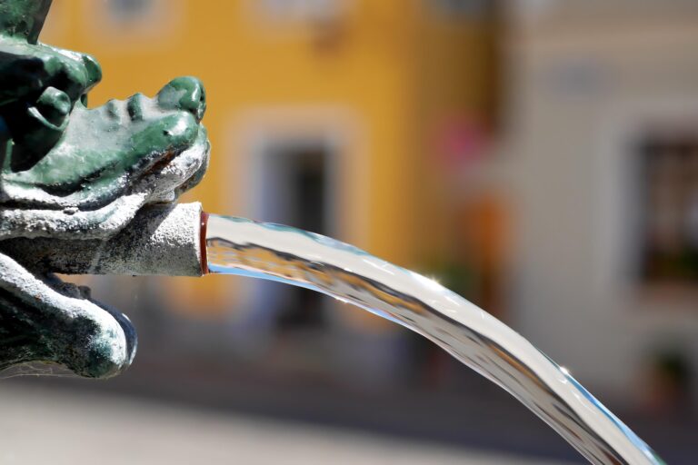 Close-up of a green dragon fountain spouting water in an outdoor plaza.