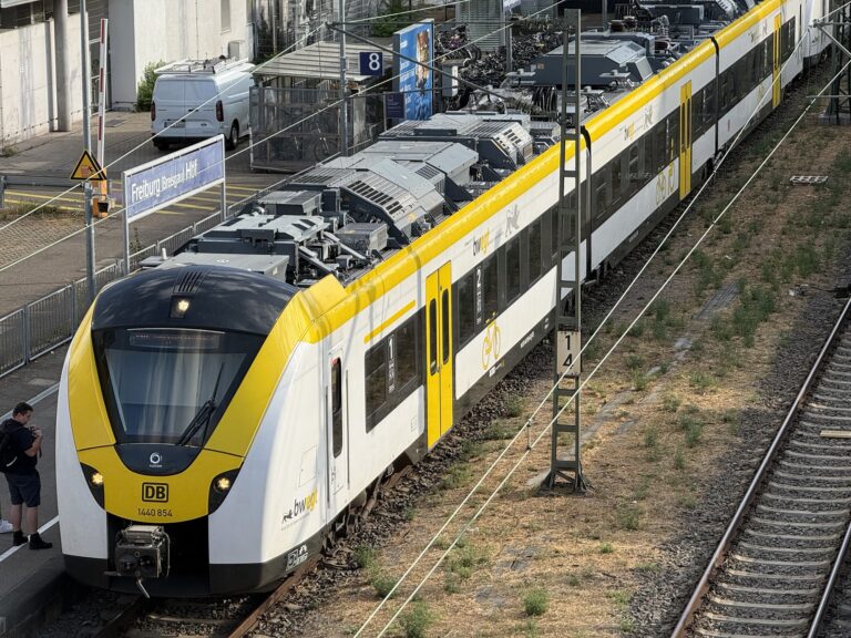 Front view of a yellow-and-white DB train at a station platform, with a person waiting nearby.