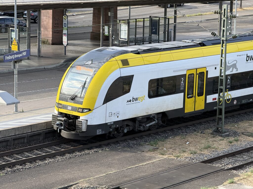 Yellow-and-white DB train at Freiburg (Breisgau) Hbf platform with track and signage visible