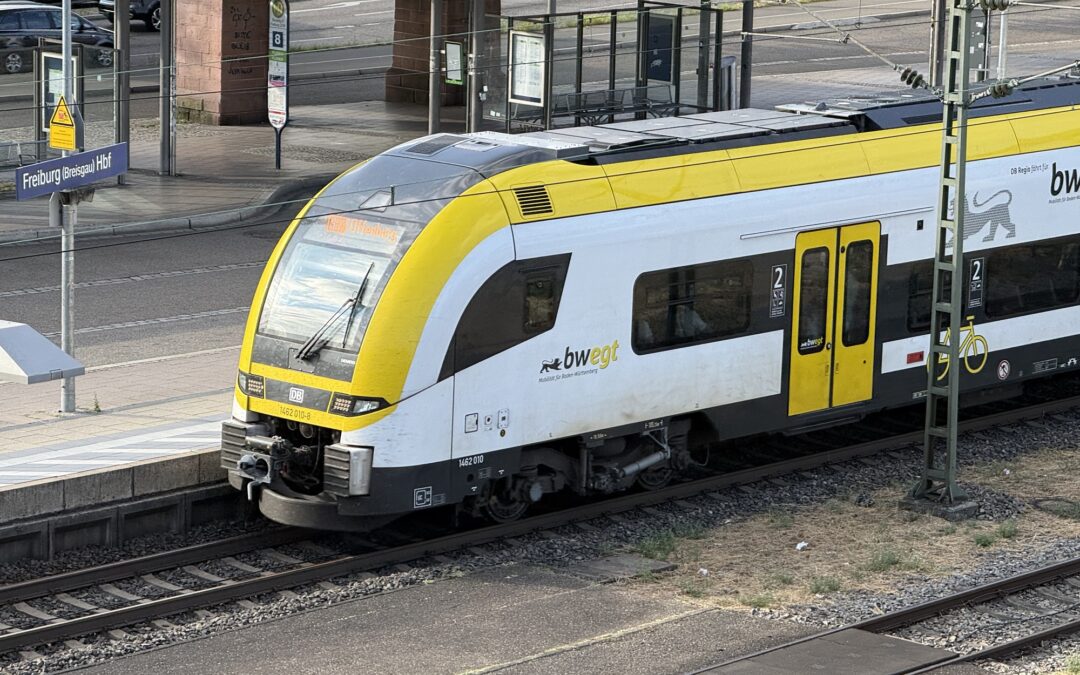 Yellow-and-white DB train at Freiburg (Breisgau) Hbf platform with track and signage visible