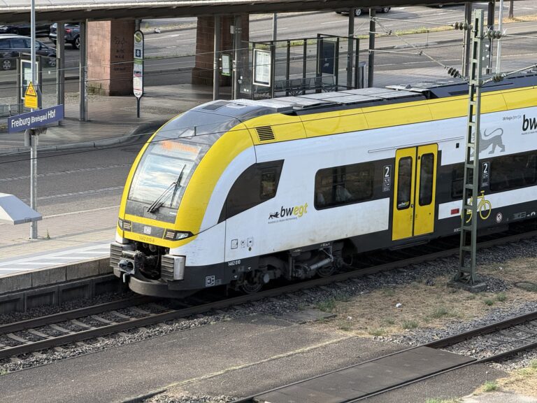 Yellow-and-white DB train at Freiburg (Breisgau) Hbf platform with track and signage visible