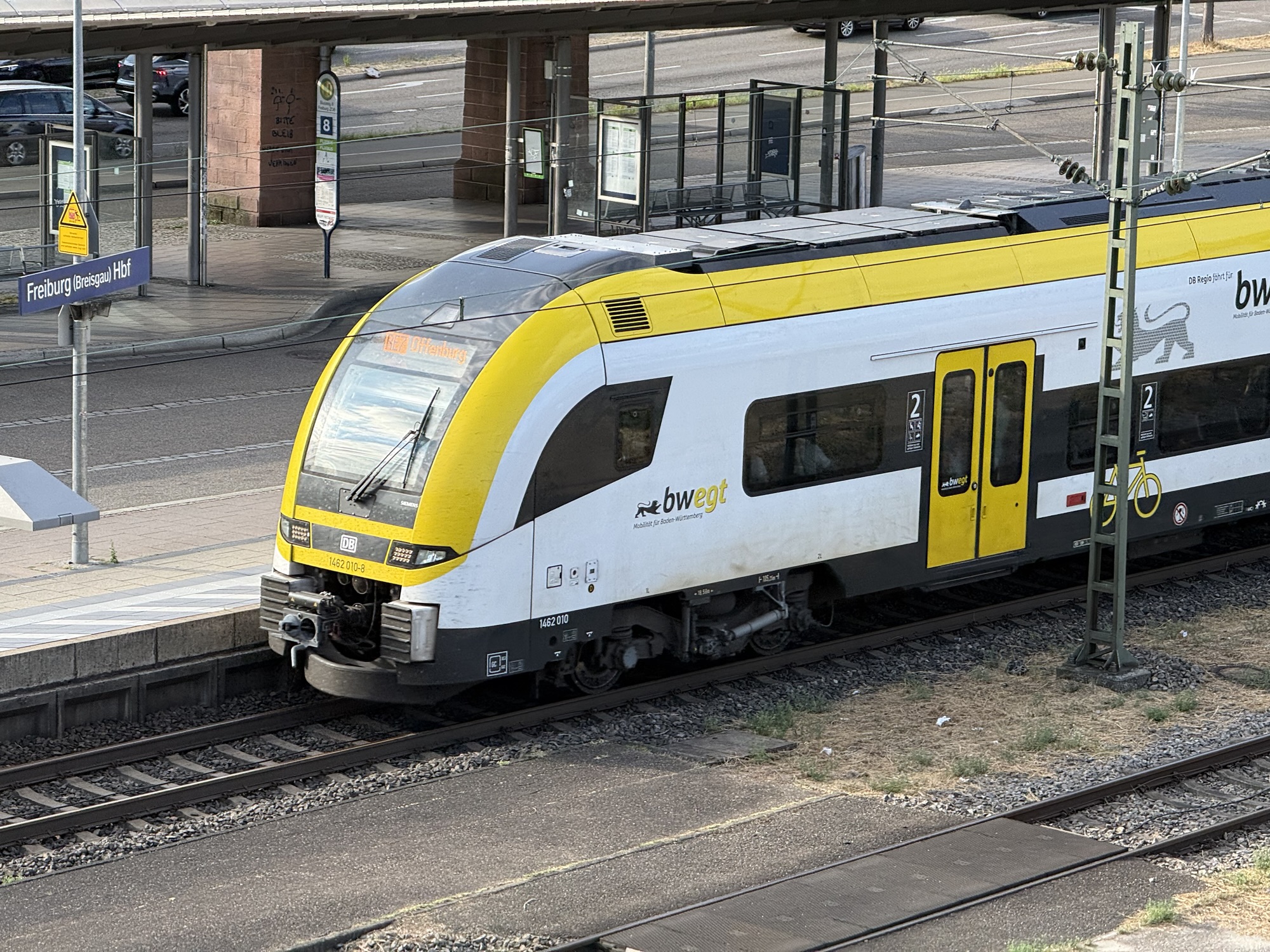 Yellow-and-white DB train at Freiburg (Breisgau) Hbf platform with track and signage visible