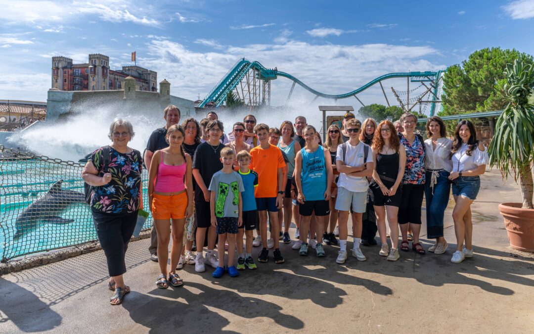 Group of smiling people of all ages posing in front of a water ride at an amusement park