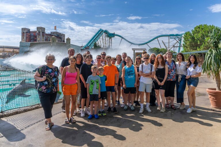 Group of smiling people of all ages posing in front of a water ride at an amusement park