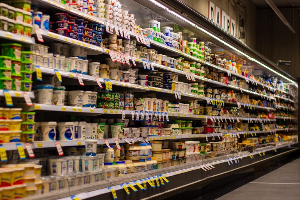 A supermarket dairy aisle with stacked yogurt cups and tubs along long refrigerated shelves.