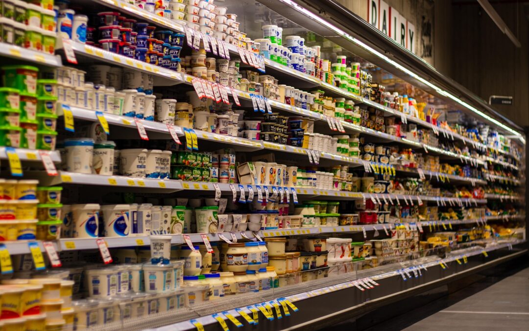 A supermarket dairy aisle with stacked yogurt cups and tubs along long refrigerated shelves.